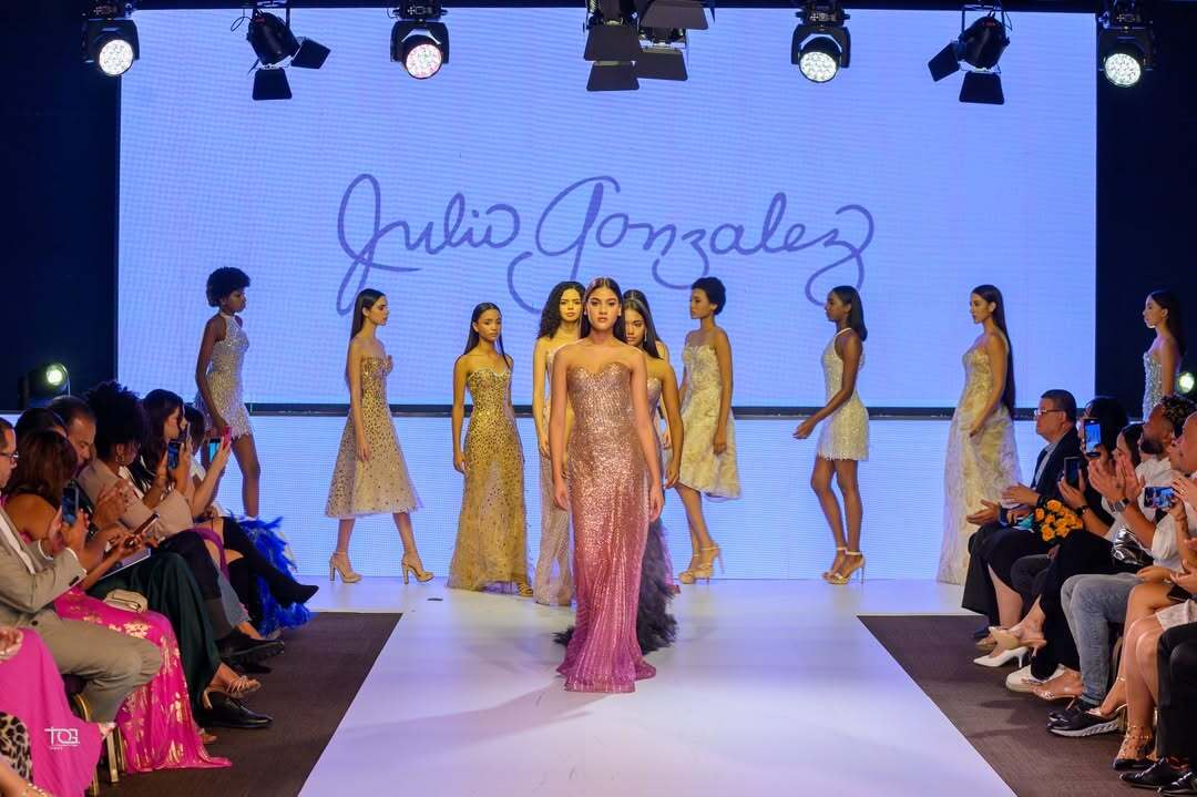 Pasarela de diseñador | Julio Gonzales en DBA Fashion Show Modelo desfila en pasarela del DBA Fashion Show con diseño de Julio Gonzales, mientras el público observa y fotografía.